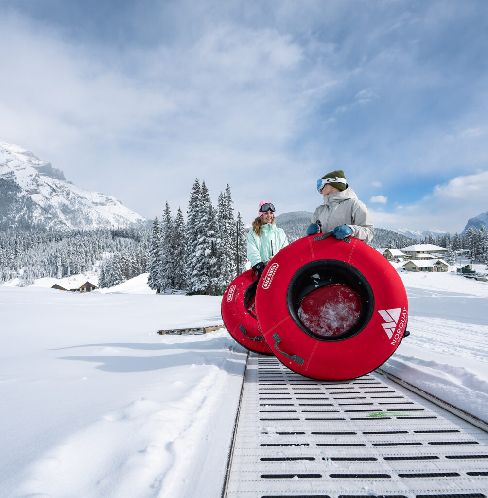Two riders on a red snow tube use Banffs conveyor lift safely.