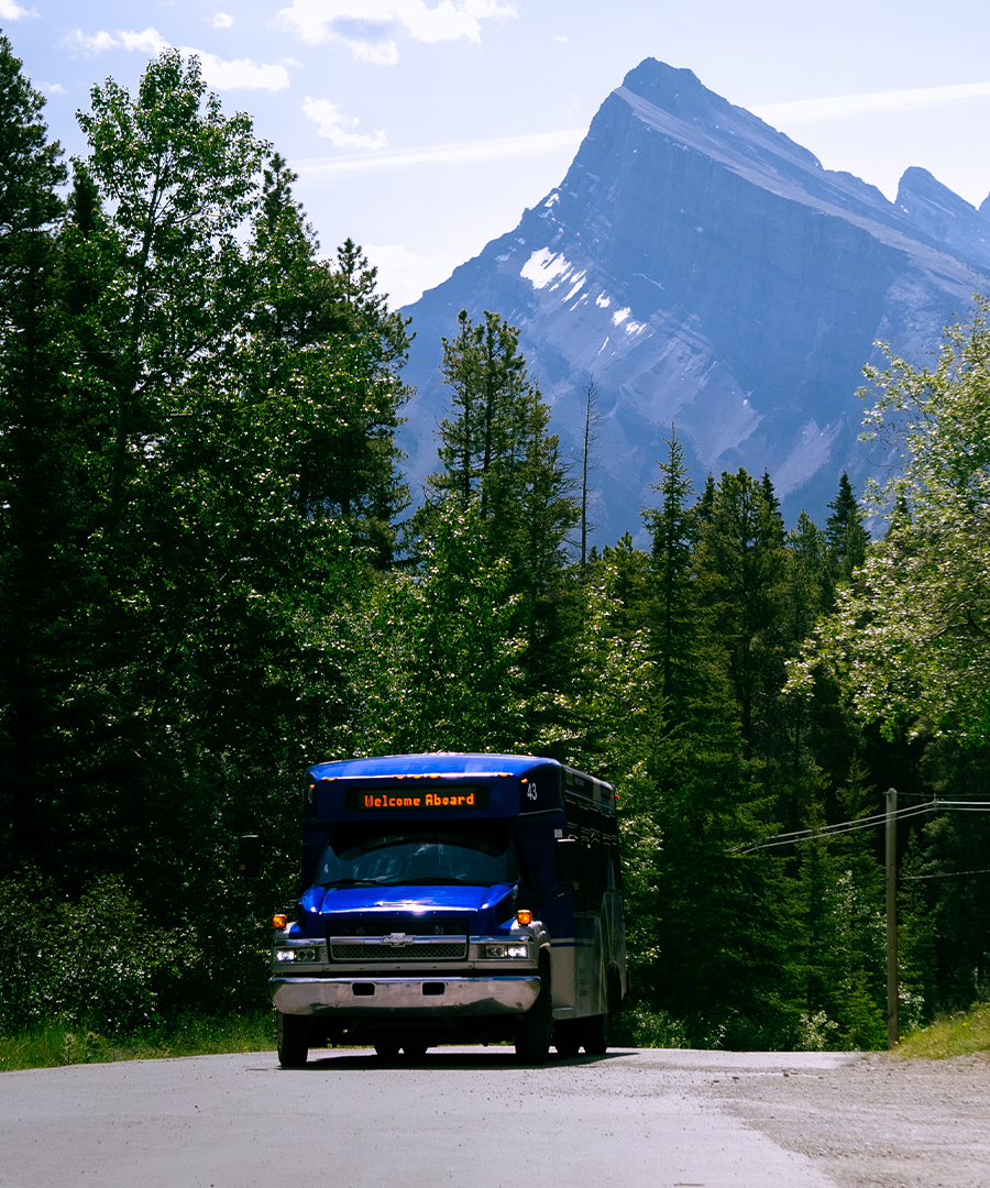 A dark blue Banff ski shuttle bus driving along a scenic Rocky Mountain road.